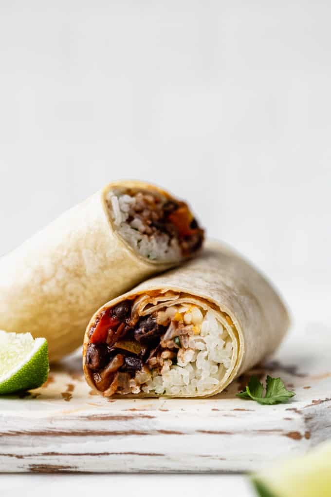 a veggie burrito cut in half with a sliced lime on the side