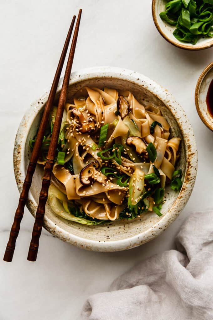 a bowl of ho fun noodles on a marble board with a napkin on the side