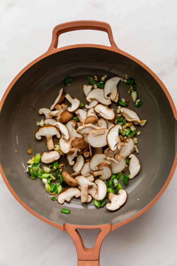 green onions, garlic and shiitake mushrooms in a pink pan