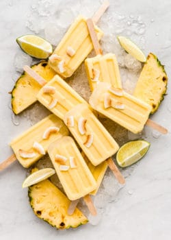 pina colada popsicles on a marble counter topped with coconut flakes