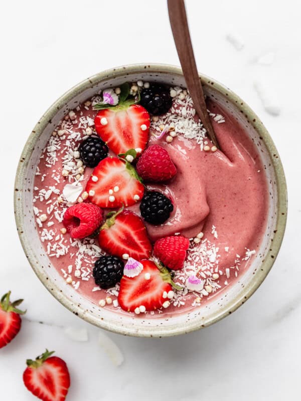a pink smoothie in a white speckled bowl topped with berries