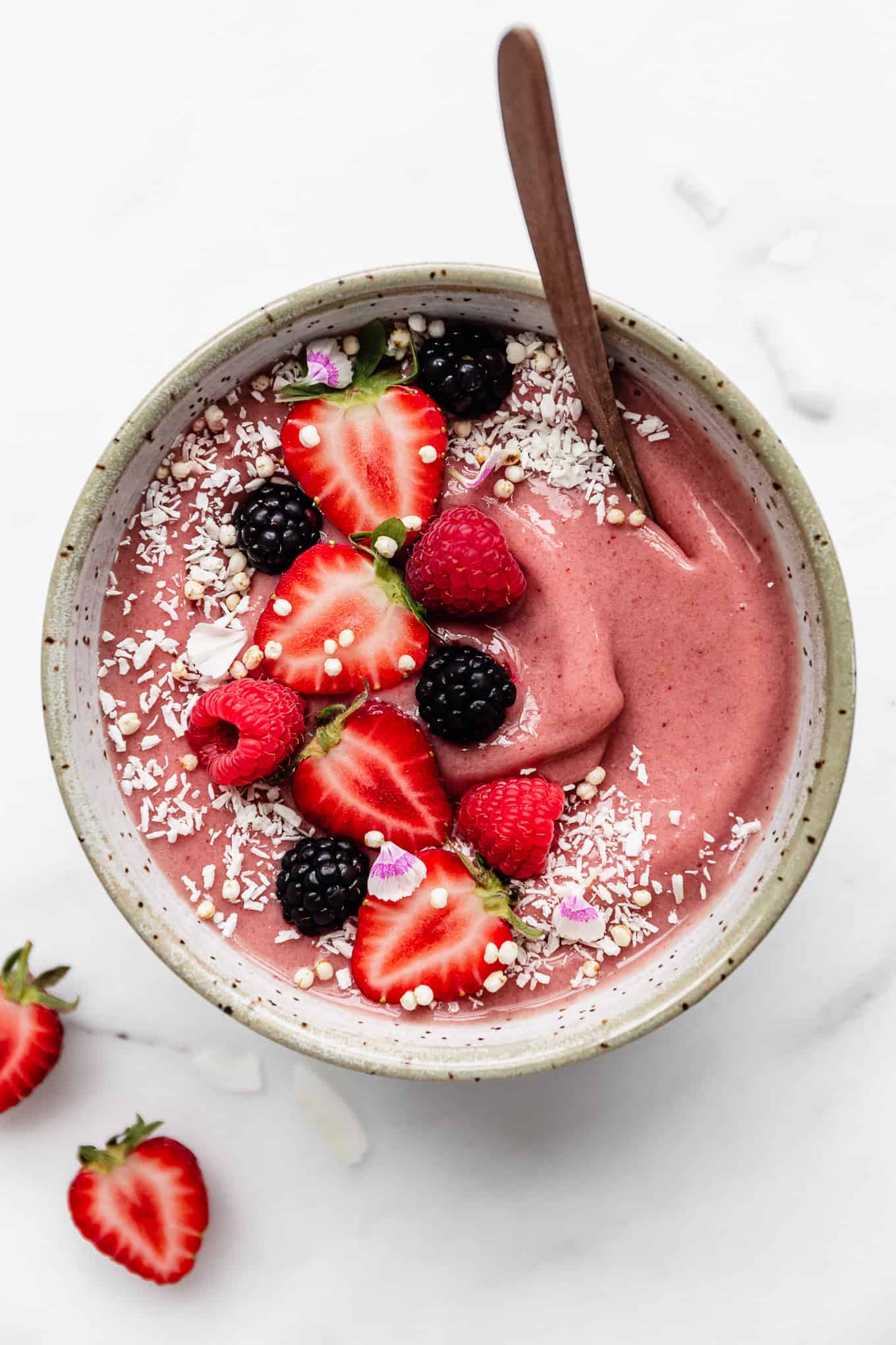 a pink smoothie in a white speckled bowl topped with berries