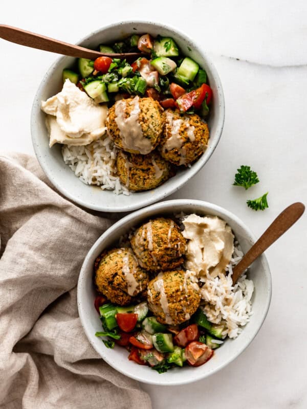 two falafel bowls with wood spoons in them