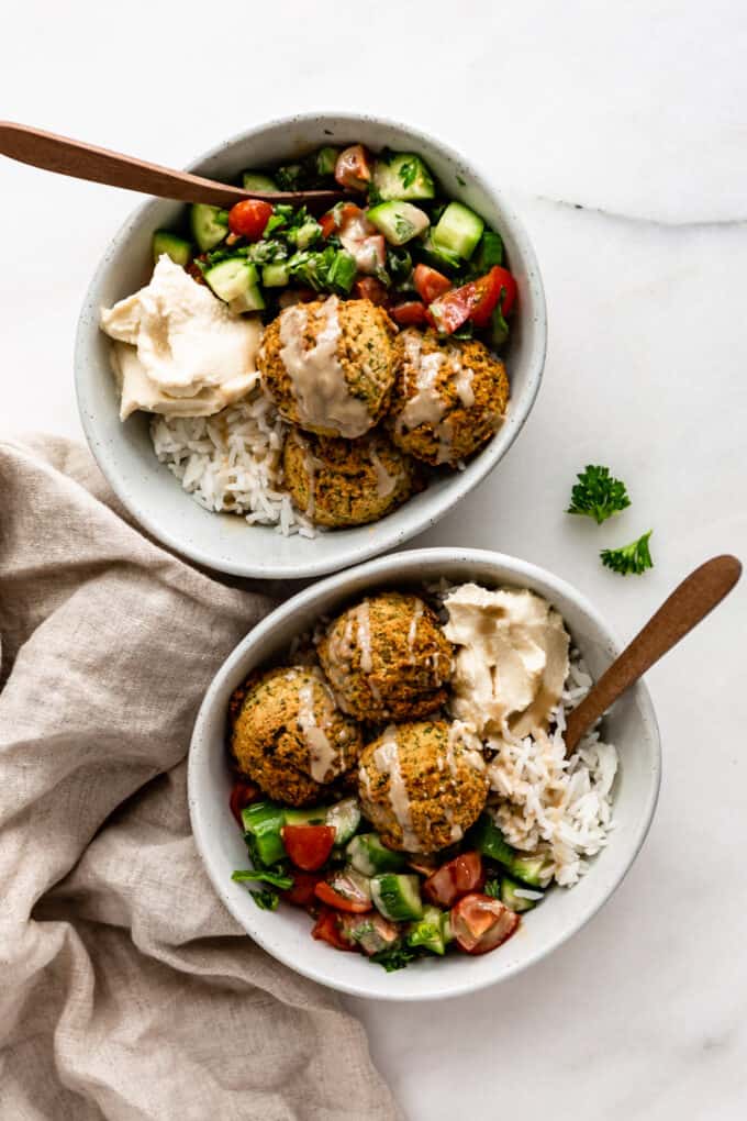 two falafel bowls with wood spoons in them
