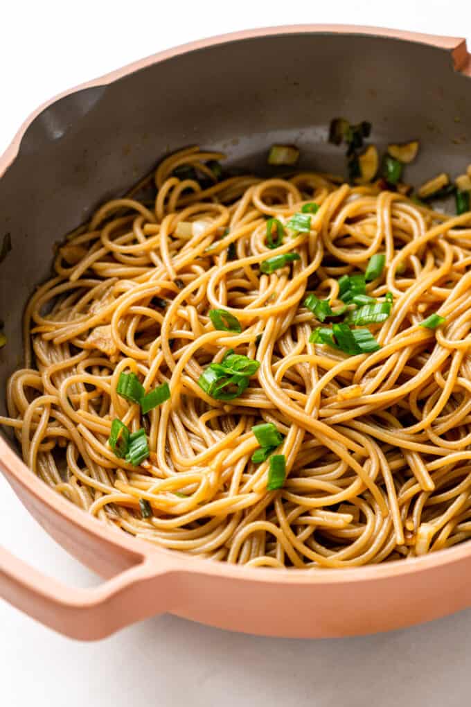 garlic noodles in a pink pan topped with scallions