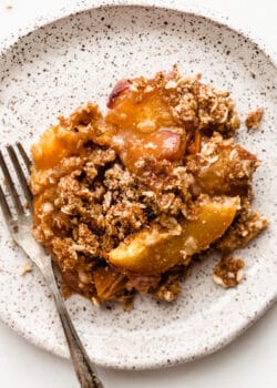 gluten-free peach crisp on a white speckled plate with a fork
