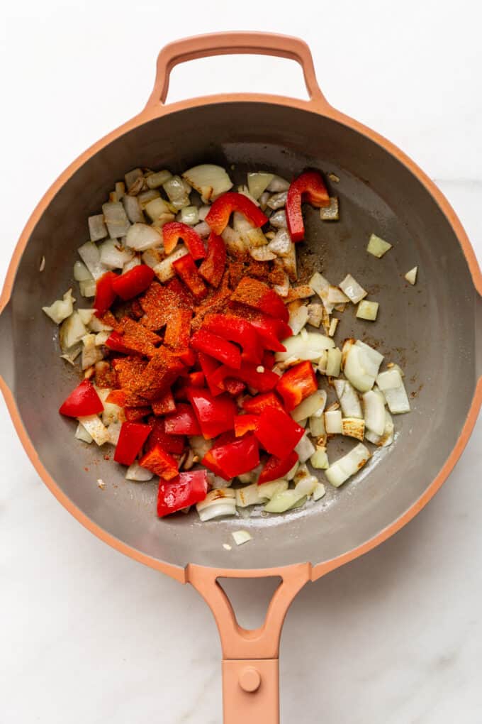 a pink pan with onions, peppers and spices in it
