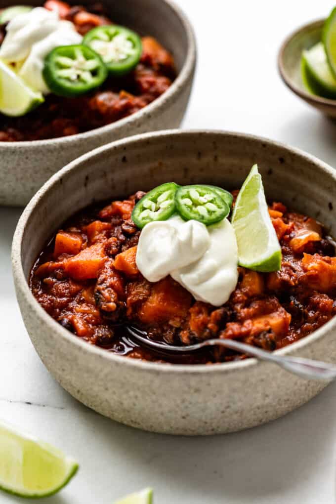 sweet potato chili in a bowl with sour cream, jalapeño peppers and lime
