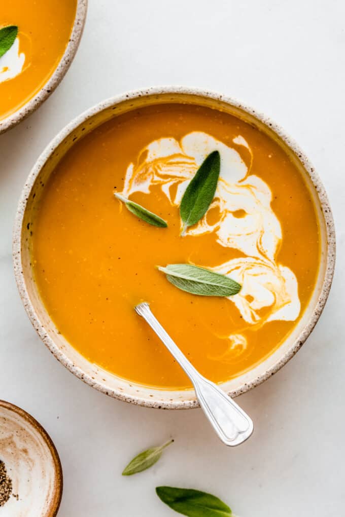 a bowl of butternut squash and apple soup topped with sage