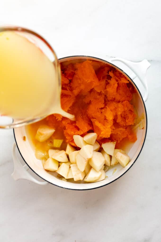 vegetable broth being poured into a pot of butternut squash and apples