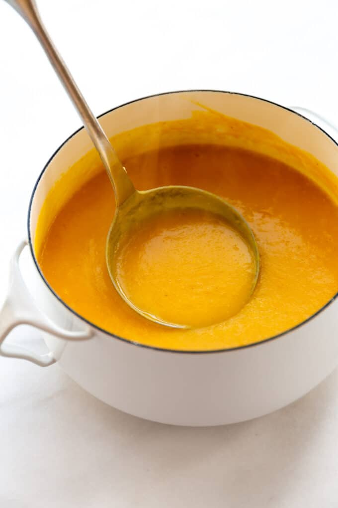 butternut squash and apple soup in a white pot with a ladle
