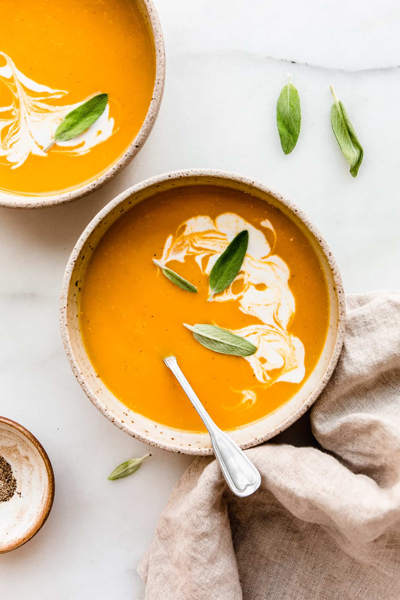 two bowls of butternut squash apple soup with a beige napkin on the side