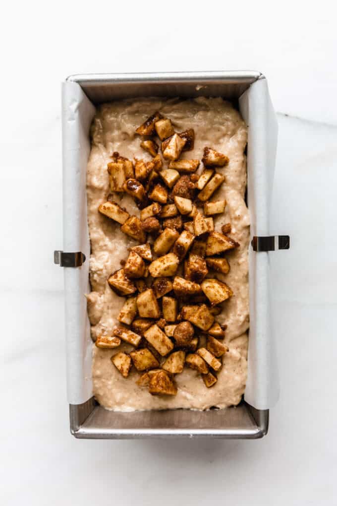 apple bread batter topped with chopped cinnamon apples in a loaf pan