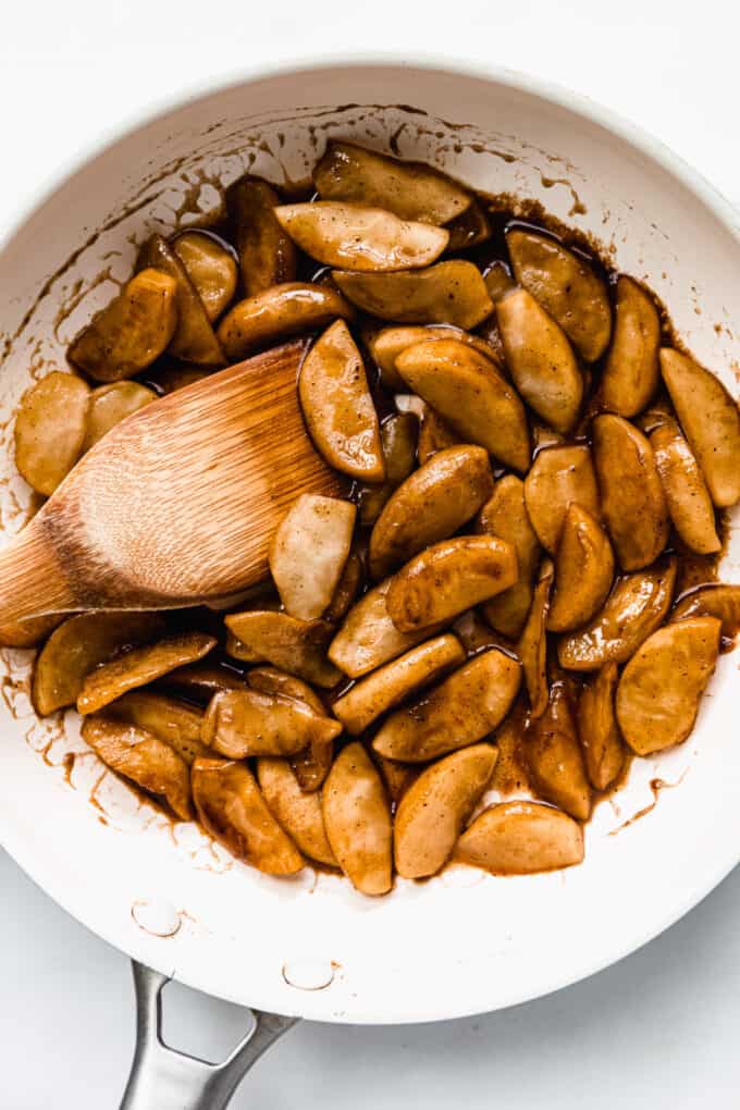 cinnamon apples in a pan with a wood spoon