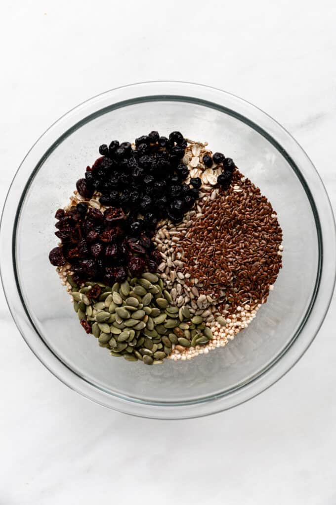 oats, puffed quinoa, flax seeds, pumpkin seeds and dried fruit in a clear bowl