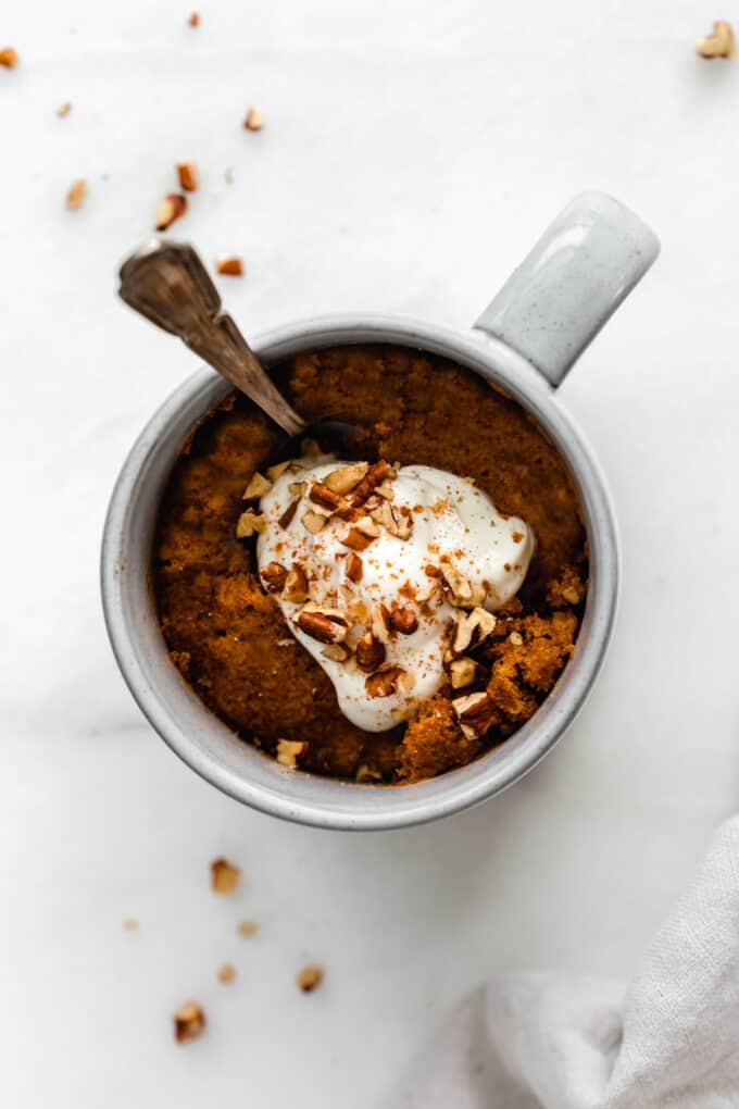 pumpkin cake topped with whipped cream and pecans in a mug