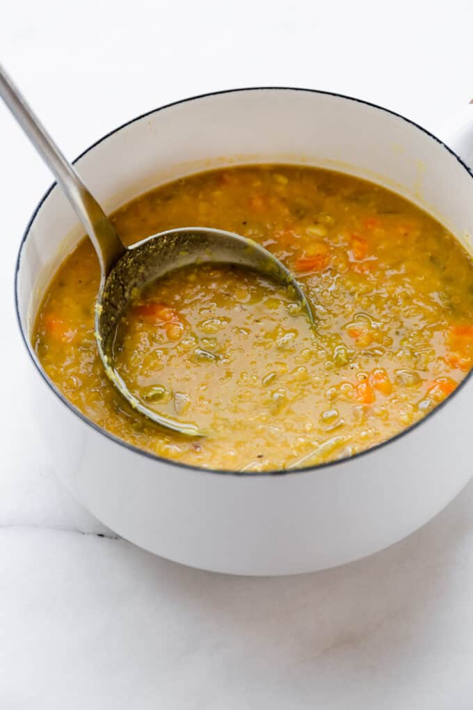 a ladle scooping red lentil soup from a white pot