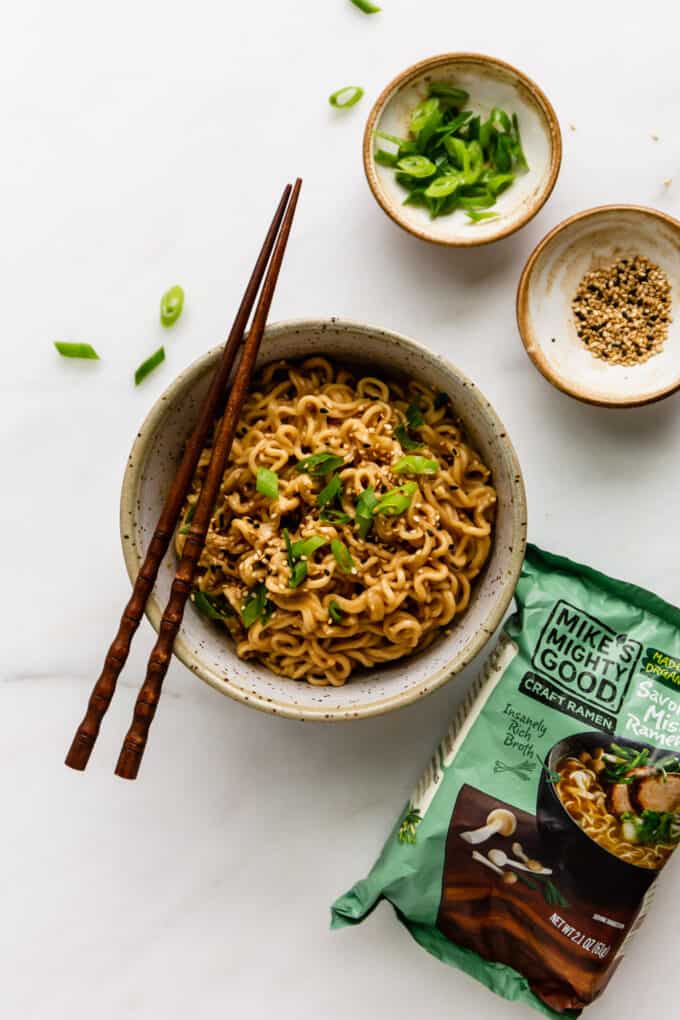 a bowl of peanut ramen noodles with a pack of ramen on the side