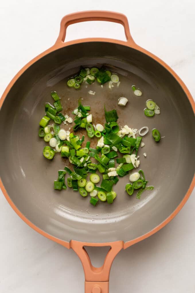 scallions and garlic in a pink pan