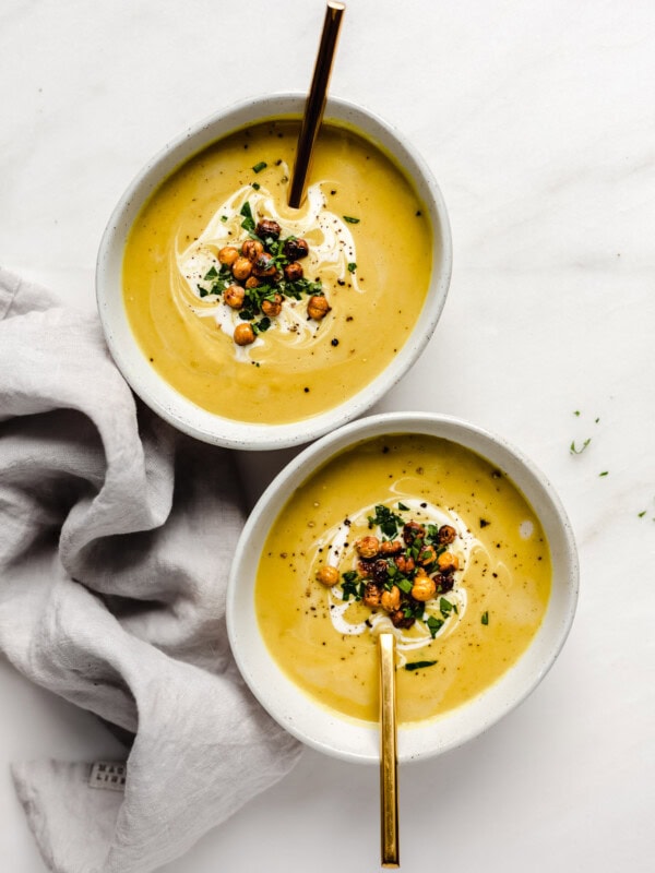 two bowls of curried cauliflower soup with gold spoons in them