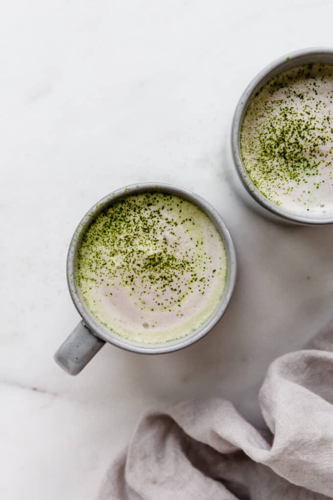 two mugs of matcha lattes topped with matcha powder
