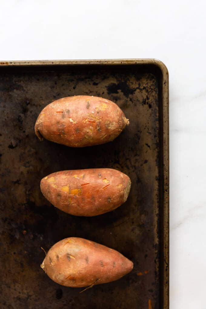 three sweet potatoes on a baking sheet