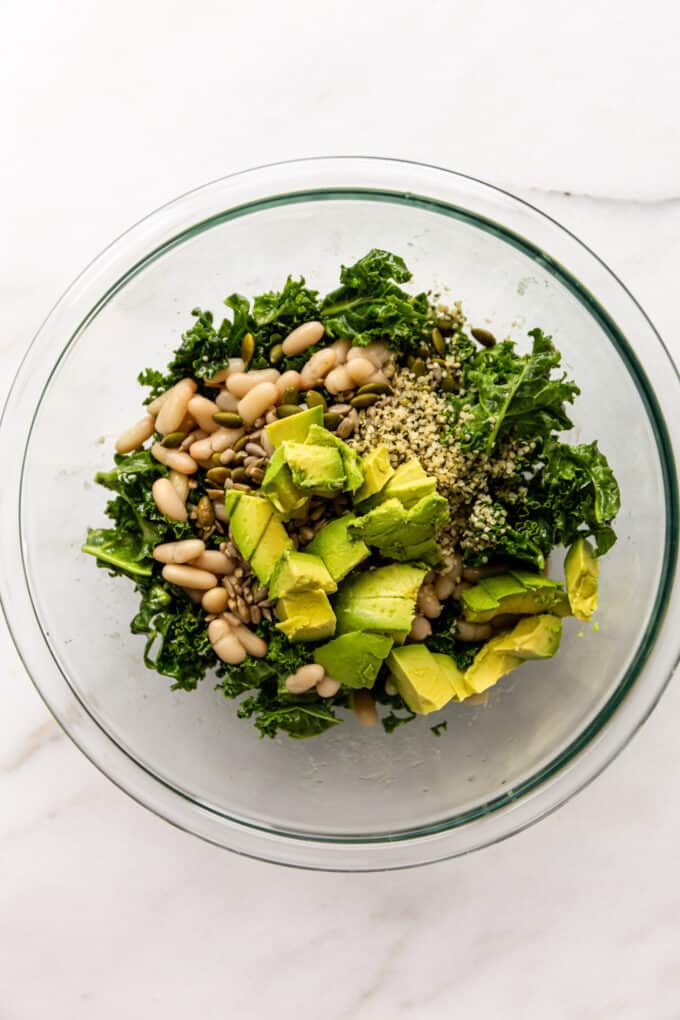 Kale, avocado, white beans and seeds in a clear mixing bowl