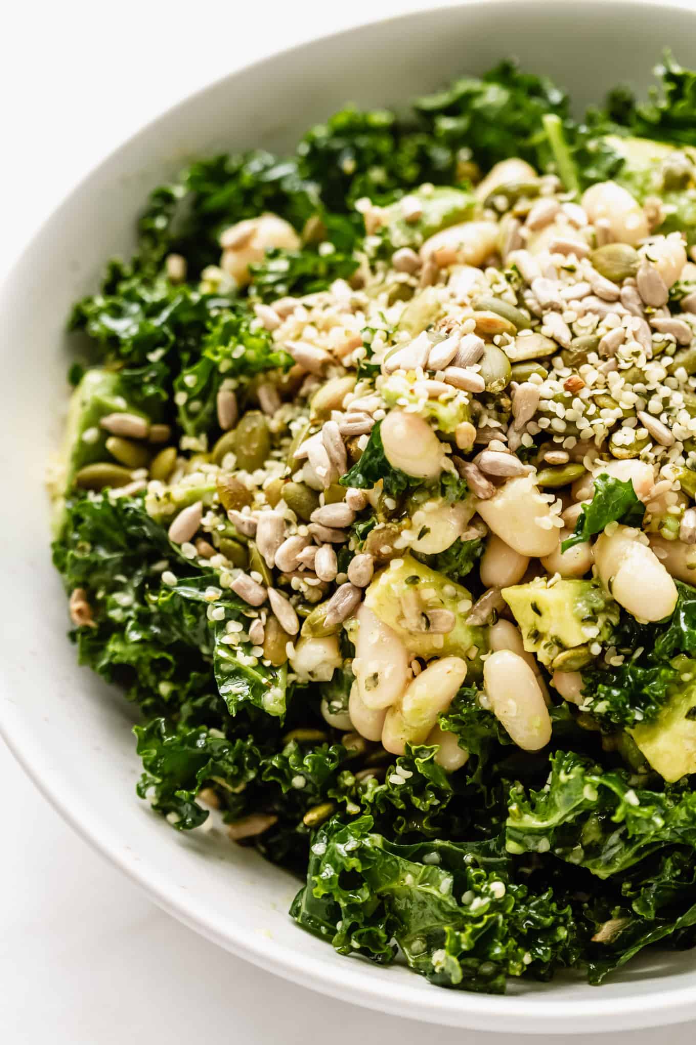 close up of kale salad in a bowl with white beans, avocado and seeds