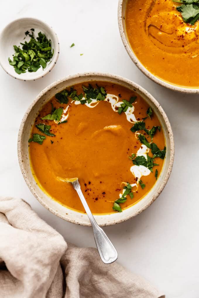 two bowls of sweet potato carrot and ginger soup with a napkin on the side