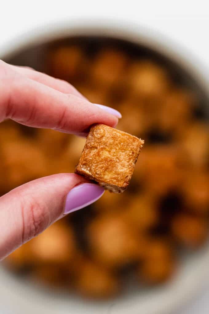 a hand holding a cube of air fryer tofu