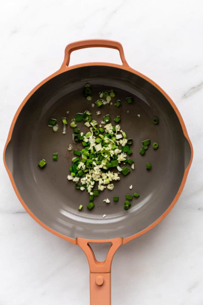 scallions and garlic in a pink pan