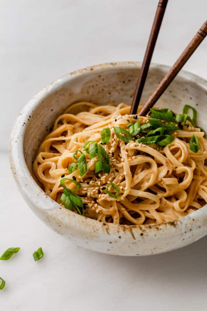 sesame noodles in a ceramic speckled bowl topped with scallions and sesame seeds