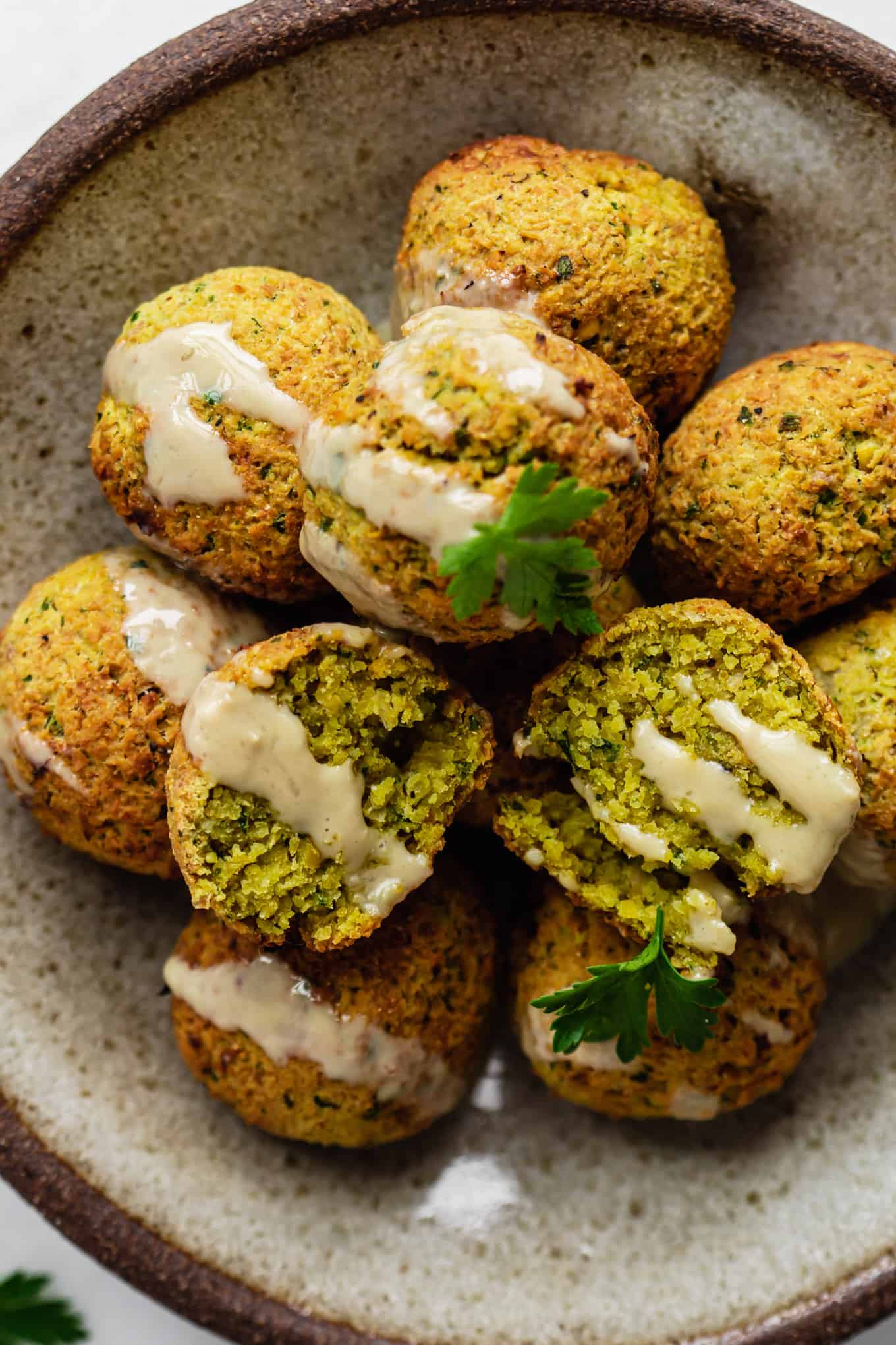 falafel balls on a plate topped with tahini and parsley
