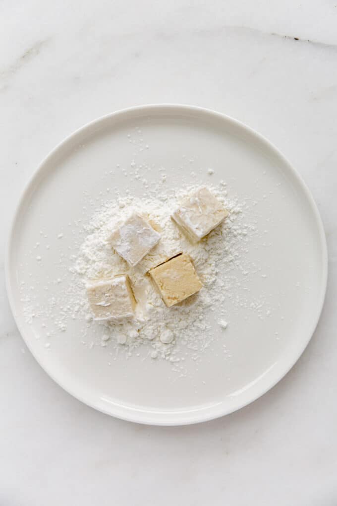 tofu cubes being dipped in a plate of cornstarch