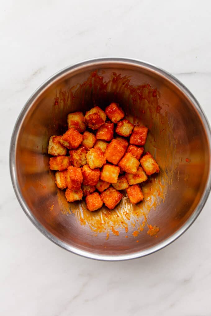 panko crusted tofu tossed in buffalo sauce in a mixing bowl