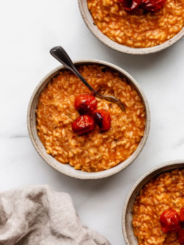 three bowls of tomato risotto topped with roasted tomatoes and basil