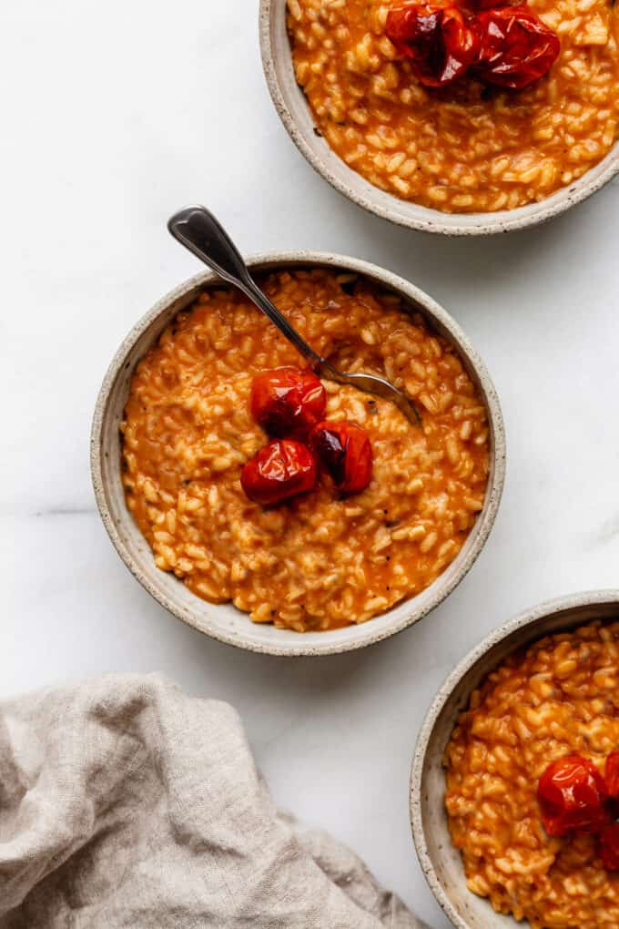 three bowls of tomato risotto topped with roasted tomatoes and basil