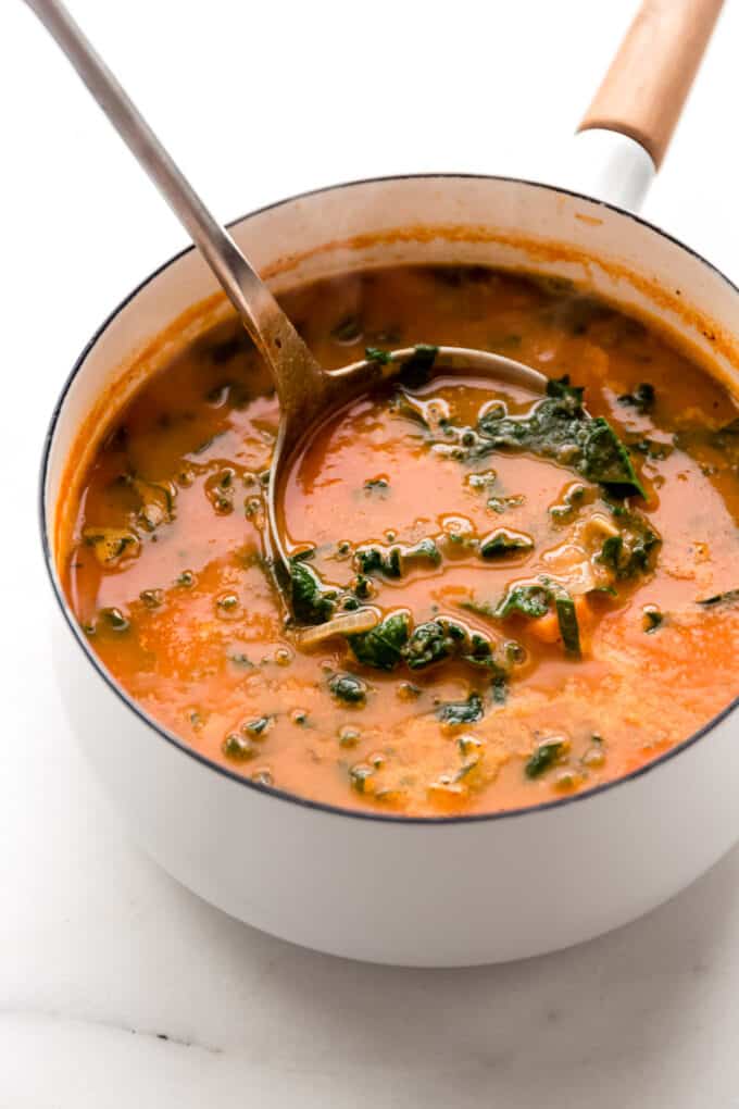 a ladle scooping white bean and kale soup out of a pot