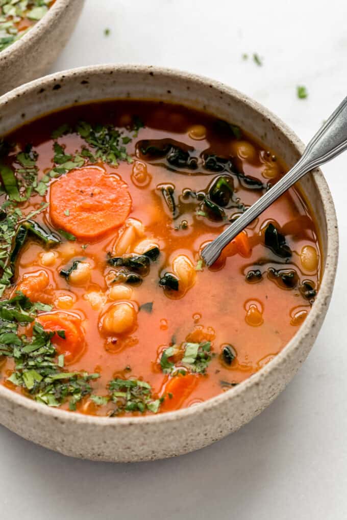 a bowl of white bean and kale soup with a spoon in it