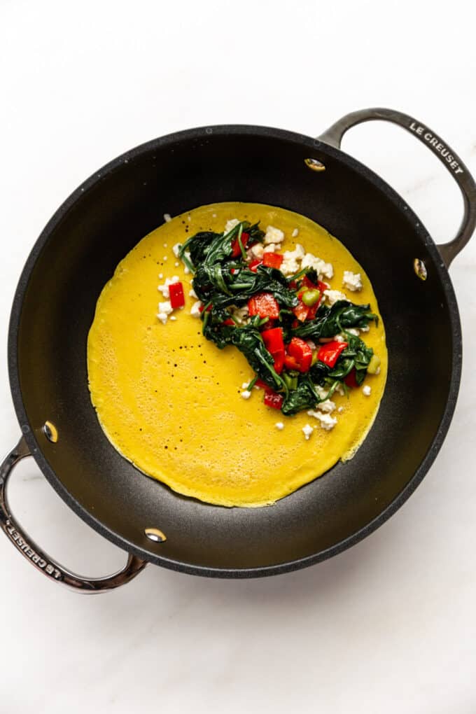 chickpea flour omelette batter in a pan with spinach, peppers and feta cheese