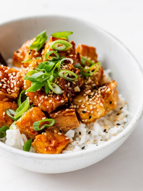 a bowl of honey garlic tofu over rice with scallions and sesame seeds