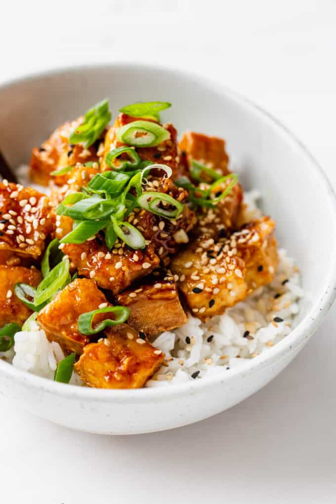 a bowl of honey garlic tofu over rice with scallions and sesame seeds