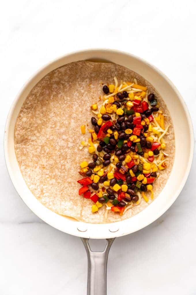 shredded cheese and black bean veggie mixture on a tortilla in a pan