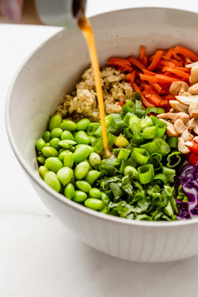 edamame salad in a large bowl with sesame dressing being poured into it