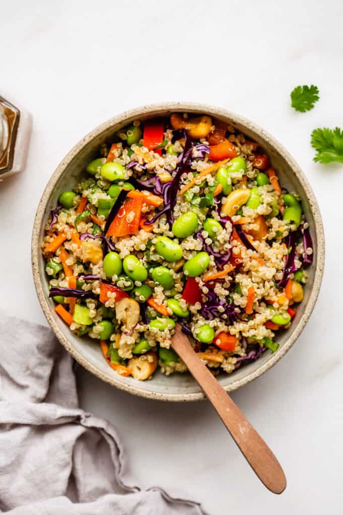 A bowl of edamame salad with a wood spoon in it