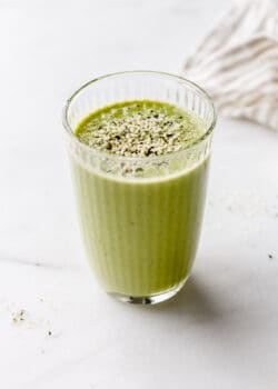 A glass of green protein smoothie with a beige napkin on the side