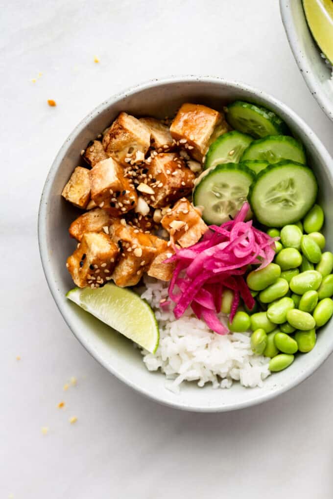 a peanut tofu bowl with cucumber, edamame and pickled onions