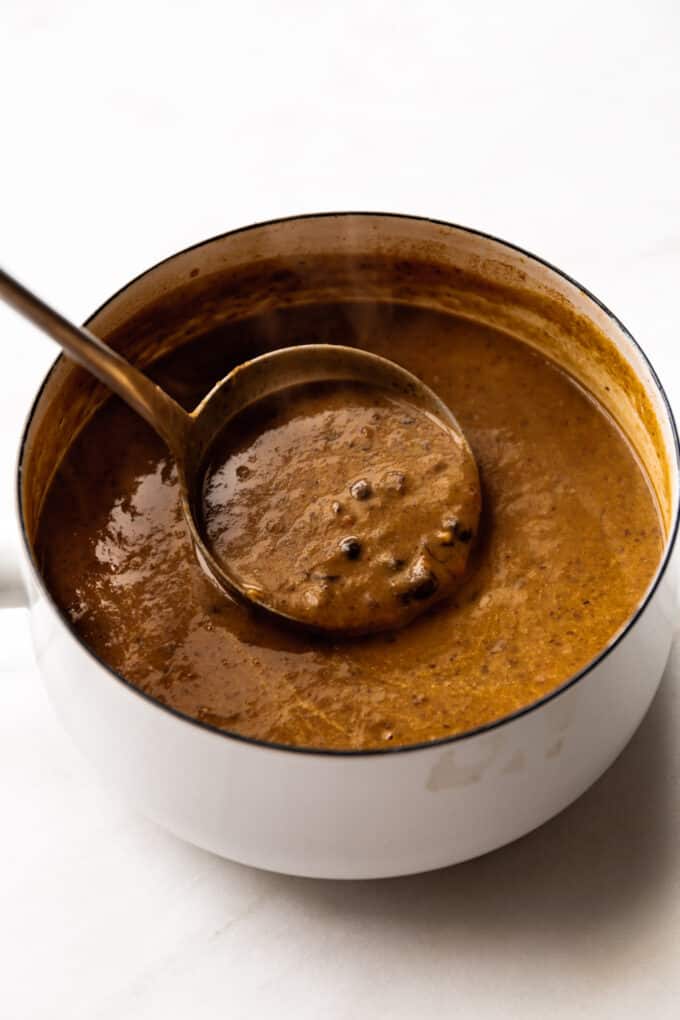 black bean soup being spooned in a ladle in a white pot