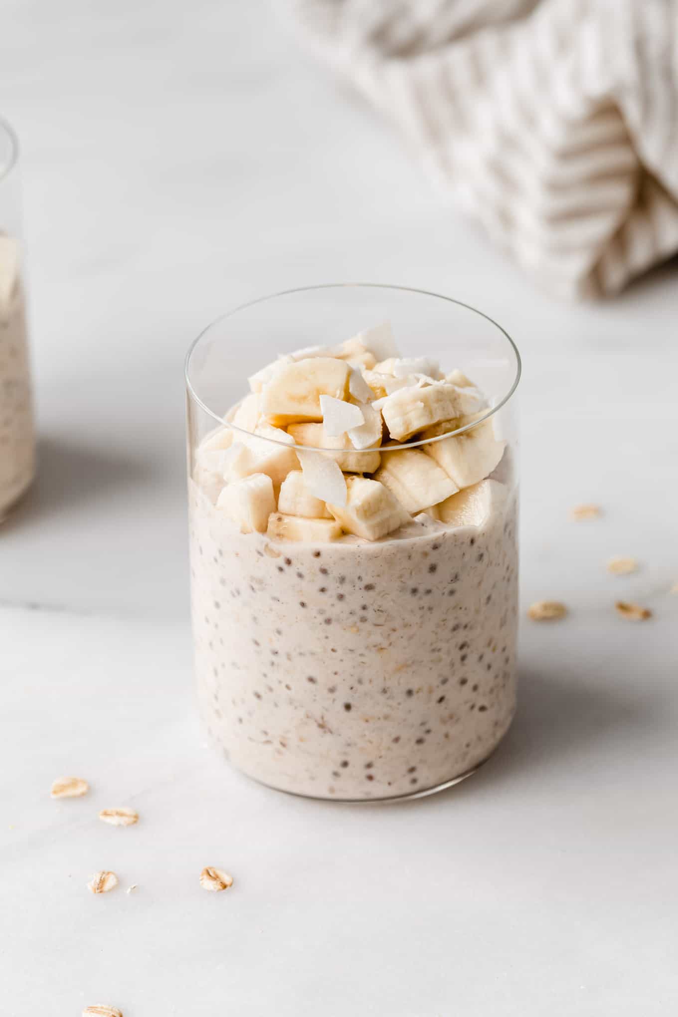 a glass of banana overnight oats topped with banana and coconut flakes.