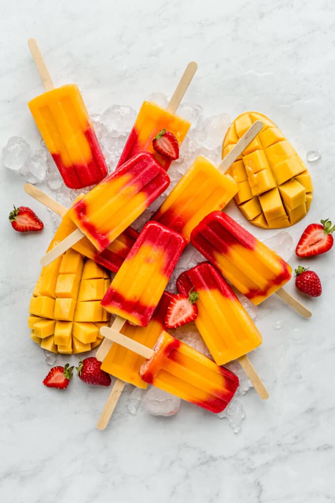 strawberry mango popsicles on a marble board with mangos and strawberries